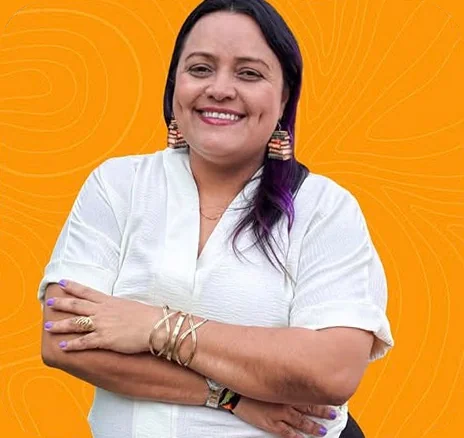 Nevys Niño sonríe con los brazos cruzados, blusa blanca y aretes artesanales